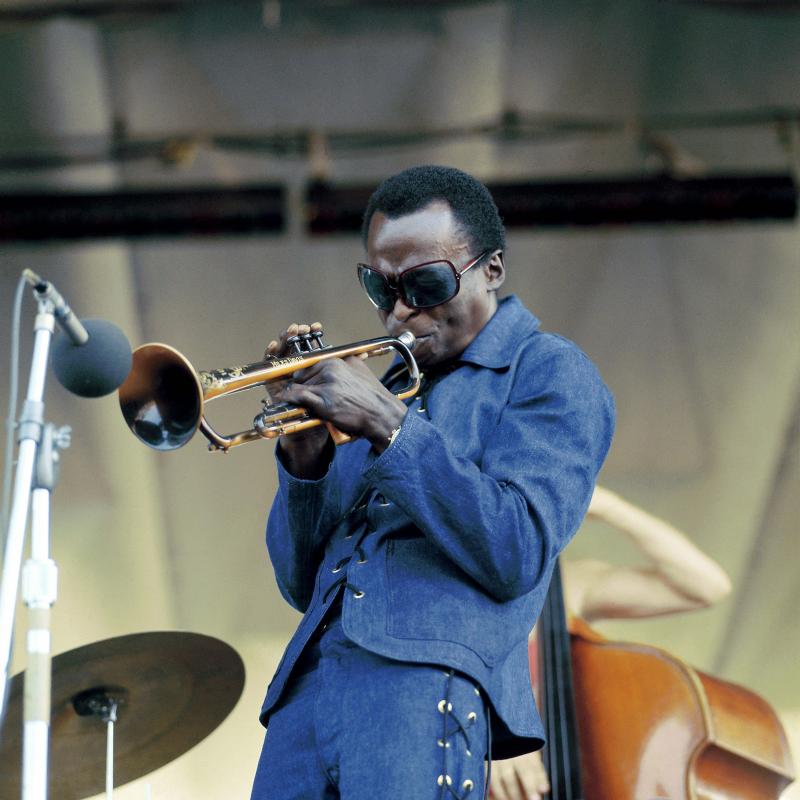 Miles Davis playing his trumpet at Newport in a jean suit with sunglasses