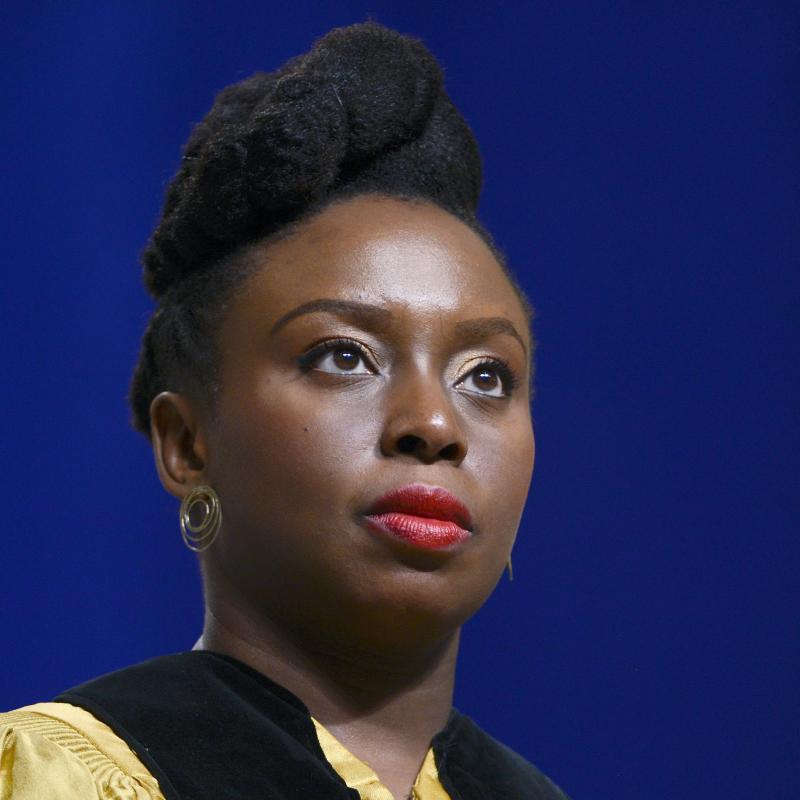 Writer Chimamanda Ngozi Adichie looks up past the camera against a dark blue backdrop
